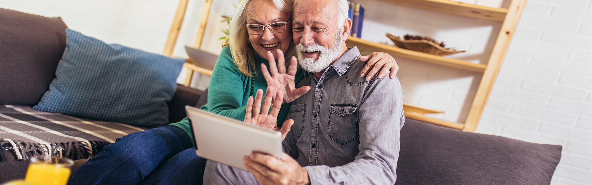 Ein älteres Paar schaut mit einem Lächeln in ein Tablet, das der Mann in der Hand hält